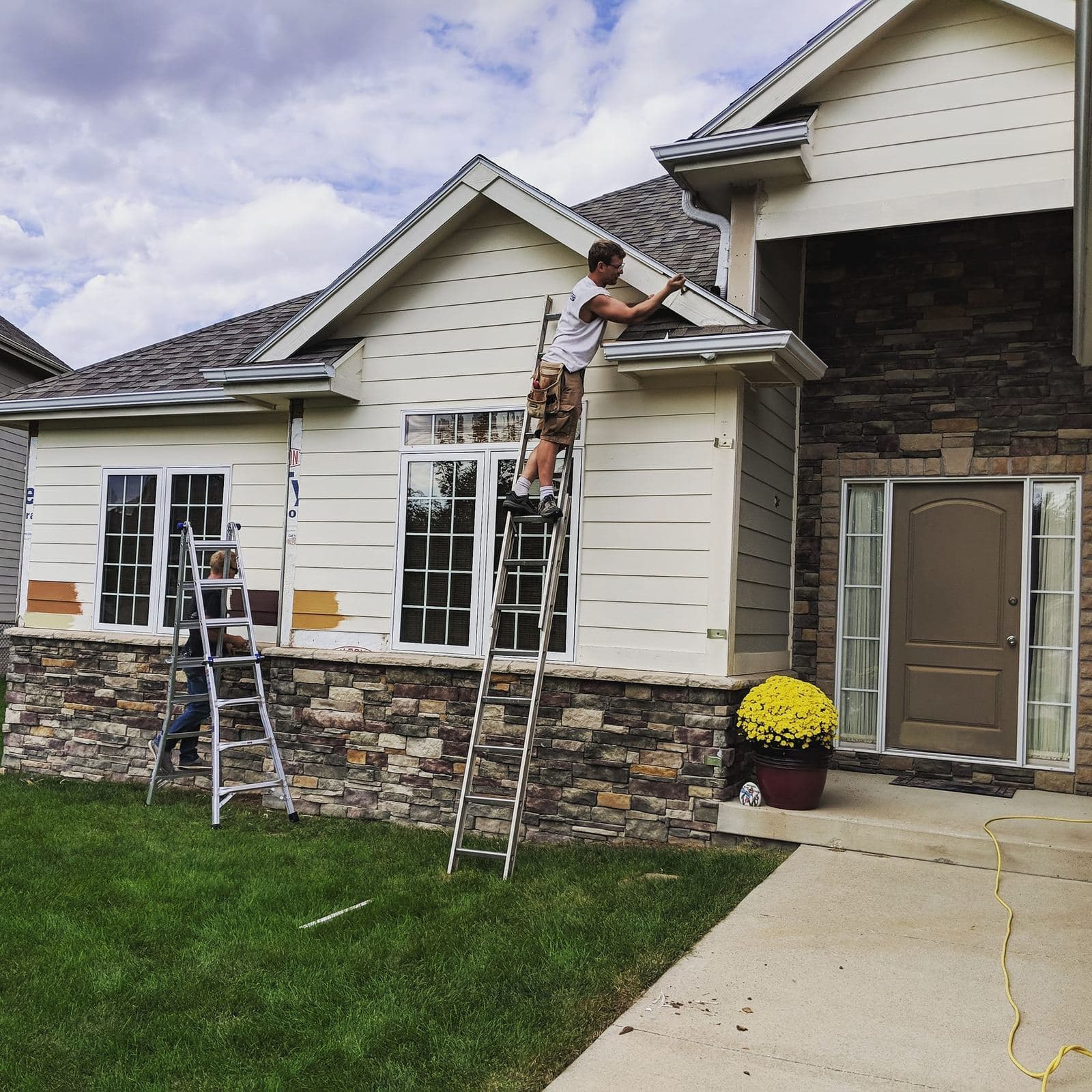 A tradesman on a ladder installing lap siding above a stone accent base on a single-story home.