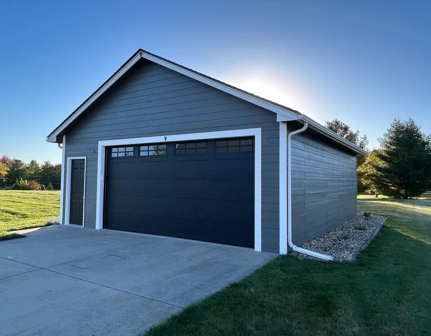 A detached garage clad in blue lap siding with white trim and a dark overhead door, finished with a concrete apron.