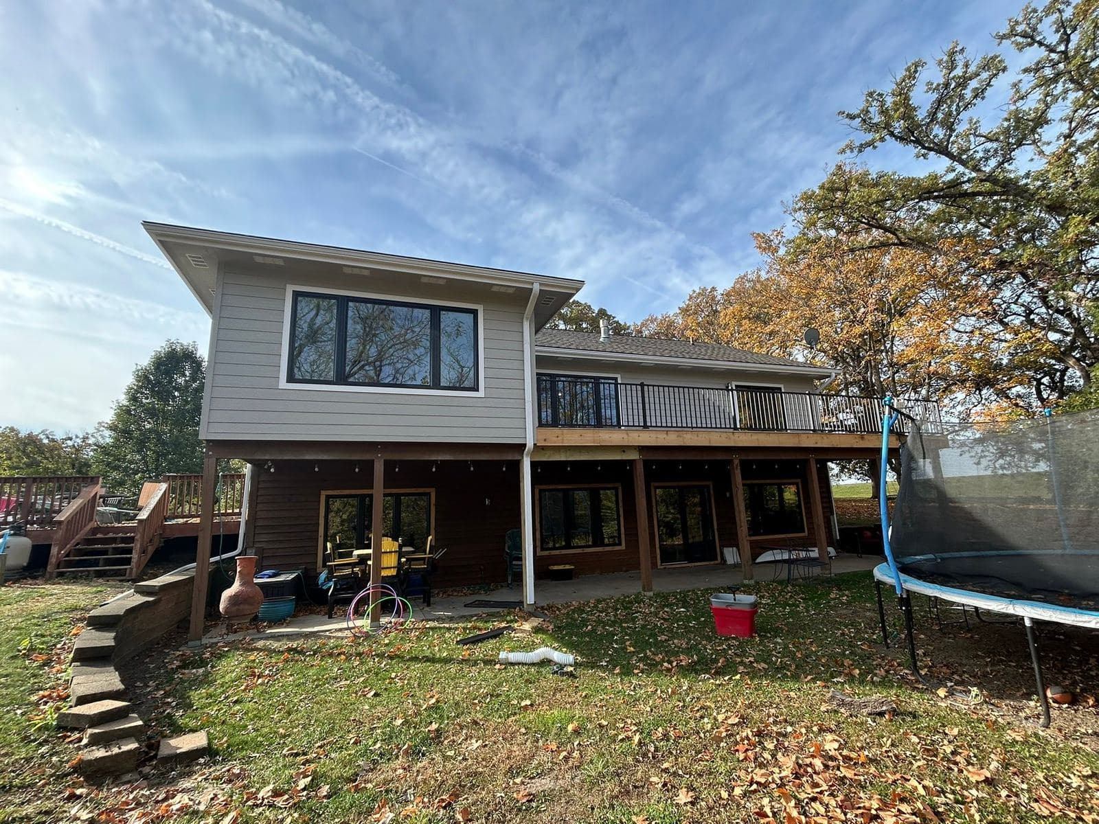 A two-tone sided home with an upper deck, photographed in autumn against a clear sky.