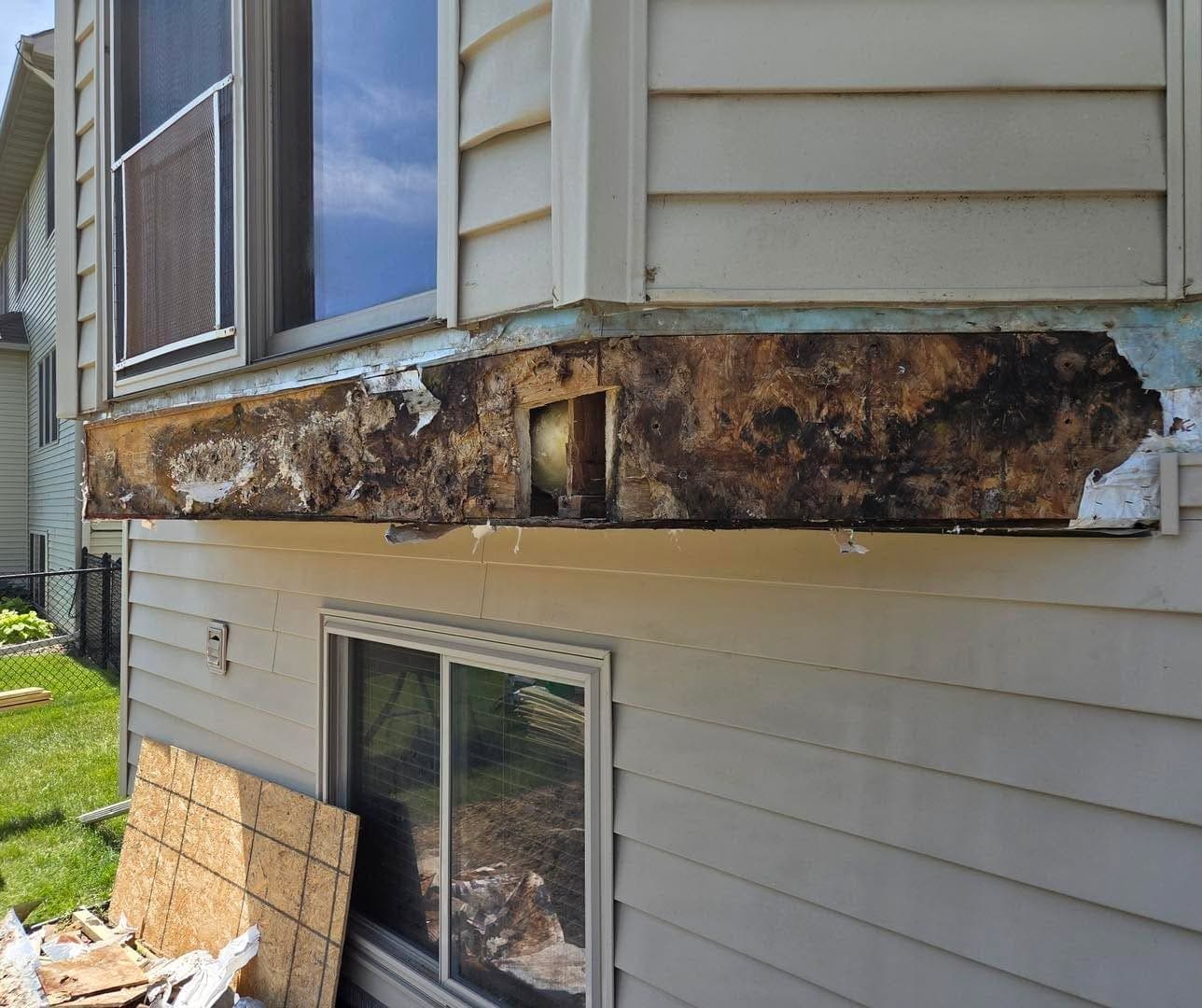 The rotted band under a bay window with the siding stripped off, showing how far the damage runs.