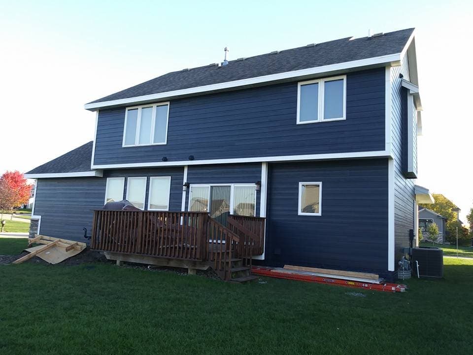 A two-story house finished in dark blue siding with white trim, and a new deck across the back.